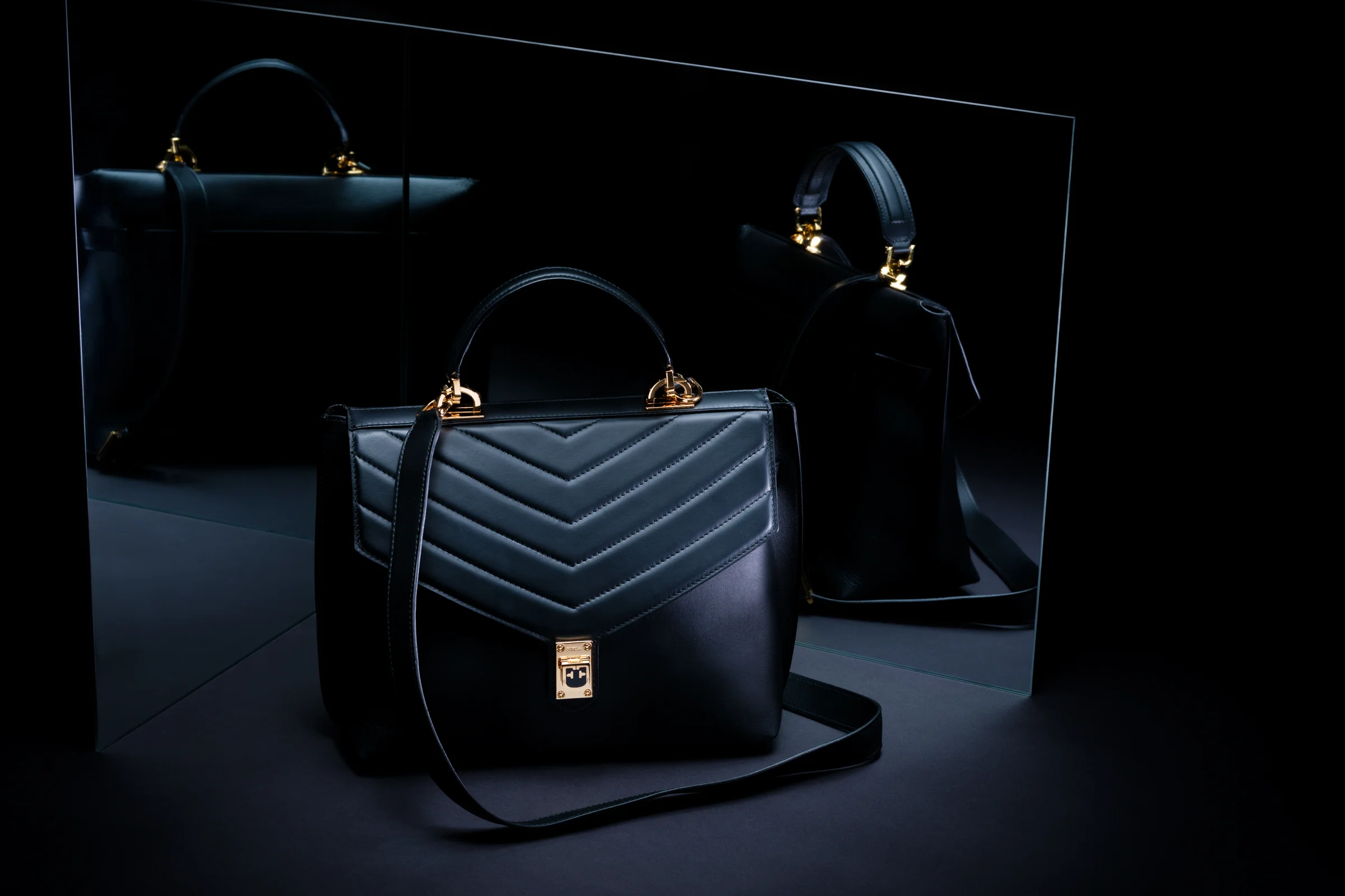 Schwarze Handtasche mit Chevron-Steppung und goldenen Beschlägen vor zwei Spiegeln